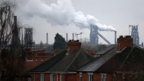 The tops of roofs in a residential area of Scunthorpe, with the steel works in the distance behind the houses.