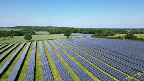 An array of solar panels stretched out across a wide field in a rural location.