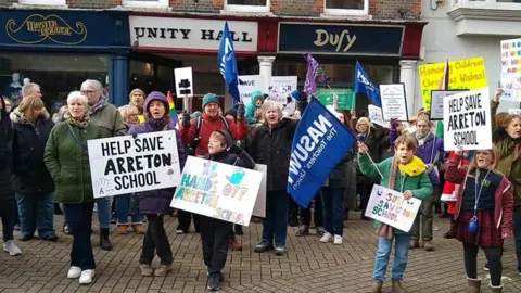 NEU A group of children and adults holding up banners and chanting in the street in Newport. Some of the banners say Save Arreton School.