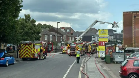 HIWFRS Three fire engines stopped on a cordoned-off road. There are hoses laid out on the pavement.