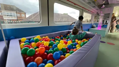 Stuart Woodward/BBC A converted railway carriage which has been turned into classroom space for a pre-school. There is a ball pool filled with colourful plastic balls, with two children inside it, as well as a colour-changing bubble tube in the background.