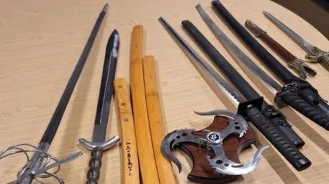 Cambridgeshire Police A table with a collection of bladed weapons, including swords, on it.