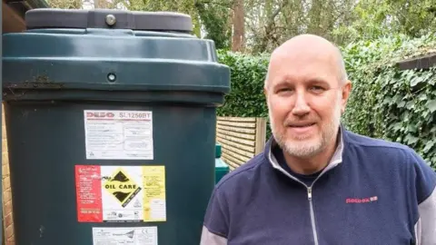A man stands next to a green heating oil tank. 