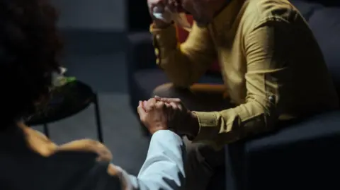 Getty Images A stock image of two people holding hands, one is holding a tissue in his other hand. 