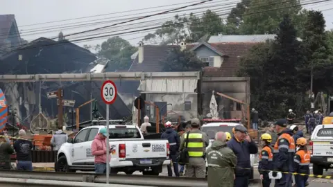 Reuters Pekerja darurat menjaga gedung-gedung yang terbakar di balik garis polisi di lokasi kecelakaan.