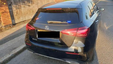 A black Mercedes car parked, with a blue police-style light in the back window