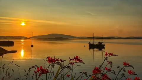 A fishing boat anchored on calm water at sunset.