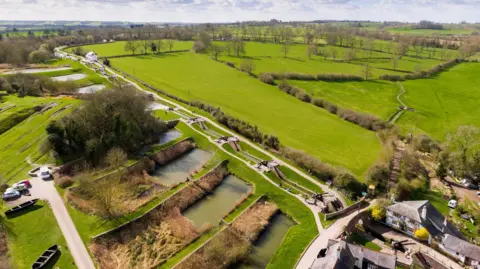 Canal & River Trust An aerial view of Foxton Locks showing multiple locks going downhill towards an area with buildings either side of the canal.