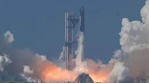 A black SpaceX Super Heavy booster carrying the Starship spacecraft lifts off.