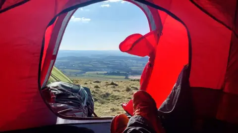 Marc Jeffrey Marc Jeffrey sitting inside a red tent. The doorway to the tent is open and exposes stunning views across Dartmoor.