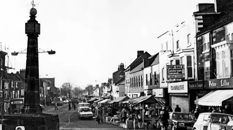 Teesside Archives/Mirrorpix/Getty Images Vintage black and white photograph of Guisborough's market, with shoppers and cars