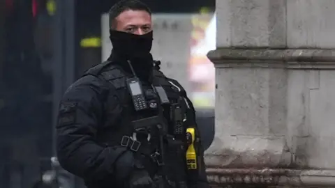 PA Media A male police officer, wearing black, face partly covered, holding a firearm.