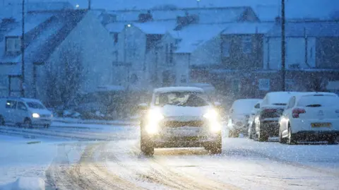 Owen Humphreys/PA Wire A car with headlights on driving in dim snowy conditions in Cullercoats on North Tyneside.