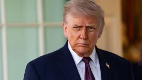 Donald Trump looks off to the side of the camera wearing a dark suit with an American flag badge