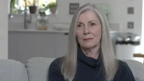 A woman with long hair sat on a grey sofa in a lounge. 