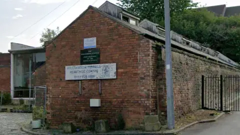 Google A single storey brick building with a white sign with blue writing which reads Williamson Tunnels Heritage Centre