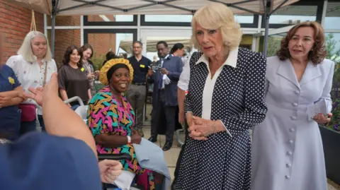 PA Media Camilla stands in a garden underneath a gazebo. There are people sitting and standing around her