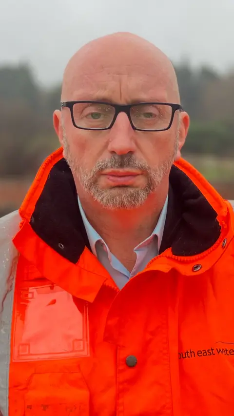 A bald man wearing glasses and a hi-vis jacket