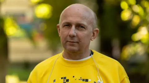 Francesco Tosto/BBC Dmytro Khyliuk stands looking into the camera, wearing a yellow shirt and headphones