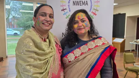 Barinder Dhaliwal Two women dressed in Saris with colour on their face 