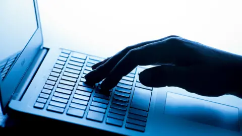 A woman's hand on the keyboard of a laptop. The hand is in silhouette and the image is tinted blue. 