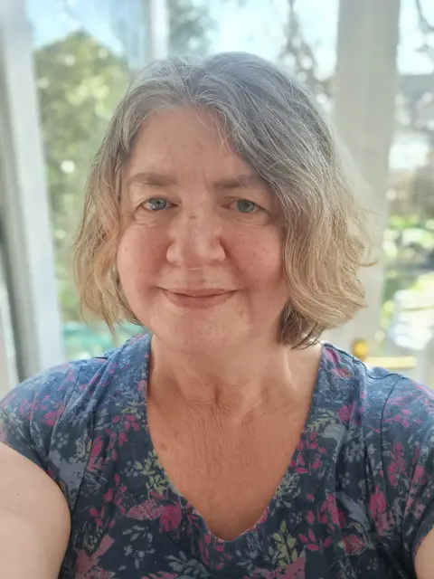 Rachel Roland Rachel Roland smiling at the camera. She has medium length wavy hair and is wearing a flowery t-shirt.
