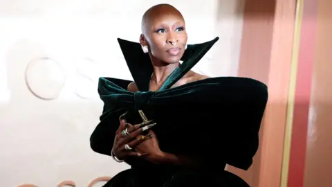 Cynthia Erivo poses during the Oscars arrivals at the 97th Academy Awards. Cynthia wears a green velvet off-the-shoulder dress. 