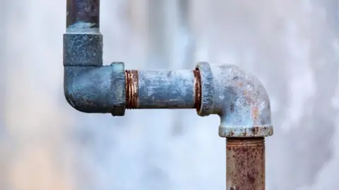 A stock image of a metal water pipe in front of a blurred background. 