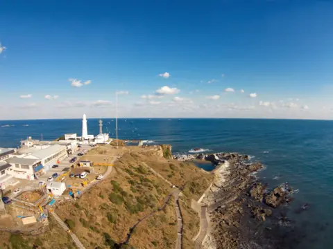 Getty Images A distant view of an outcrop of land with a lighthouse at the end looking out over a vast expanse of water