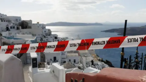 Getty Images An image of Santorini's white picturesque buildings with red tape. 