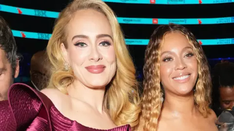 Adele and Beyonce stood beside each other smiling and posing for photographs