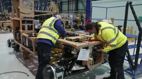 Two workers helping build a military vehicle. The vehicle is on an assembly line.