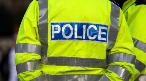 A police officer in a high visibility jacket with police logo