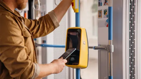 A man taps his phone against a payment pad on a bus