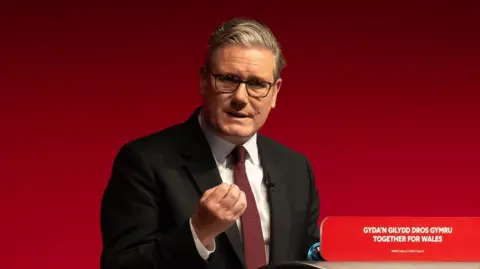 UK Prime Minister Sir Keir Starmer speaks at a lectern in front of a red background.