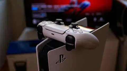 A PlayStation 5 controller balanced on the console. A TV is visible in the background.