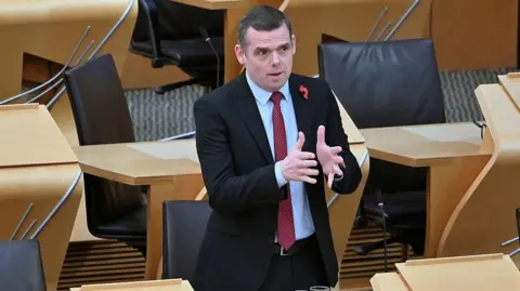 Getty Images Douglas Ross, in dark suit with blue shirt and burgundy tie, is standing up in parliament. He is gesturing with both hands, clearly making a point in a debate.