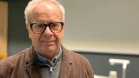 Jon Wright/BBC A man with glasses, standing in a lecture theatre