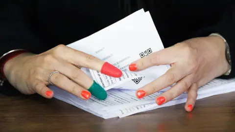 A close up image of ballot papers being counted by hands wearing thimbles on index and middle fingers and bright red nail polish, in Romford on Friday.