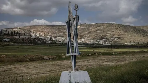 AFP File photo showing a metal Star of David placed outside the Malachei HaShalom settler outpost near the Palestinian village of al-Mughayyir (in the background), in the occupied West Bank (20 April 2026)