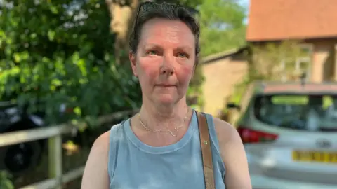 Owen Sennitt/BBC A woman looks towards the camera outside a building while wearing a blue vest