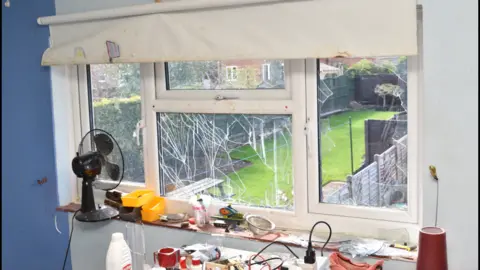 A smashed window inside the house with chemicals on a table