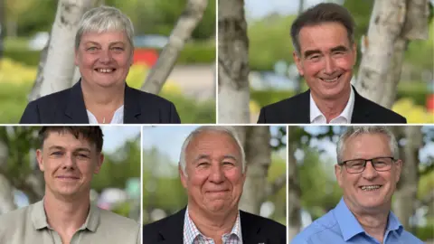 BBC Representatives of the five main parties taking part in this week's local elections for Wokingham Borough Council are pictured standing outside. They're all standing in the same location with blurred out trees and branches behind them.