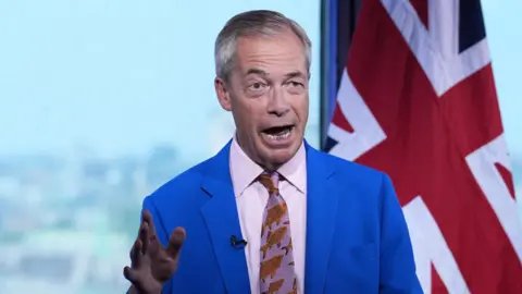 PA Media Reform UK leader Nigel Farage speaking in a bright blue suit and a purple shirt and tie with orange fish on it, with the United Kingdom flag in the background.