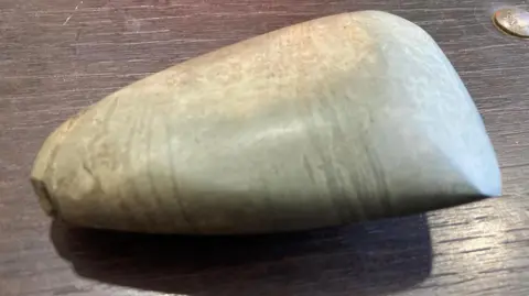A close-up photograph of a stone axe head which is polished and smooth