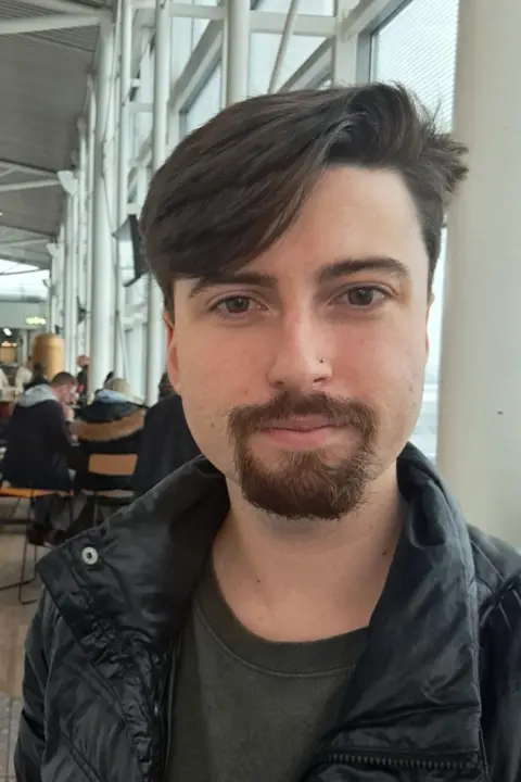 Richard Green Richard Green at Newcastle Airport. He has dark hair brushed to one side and a goatee beard. He is wearing a black jacket and a dark top.