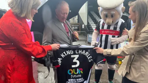 King Charles is presented with a Grimsby Town shirt inside the Blundell Park ground by the club's mascot, the Mighty Mariner.
