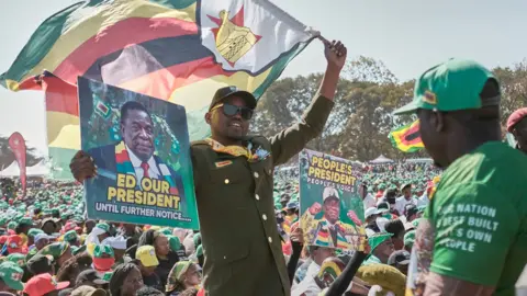 AFP A supporter of Zimbabwe's ruling party Zanu-PF holds up an election campaign poster during a rally addressed by President Emmerson Mnangagwa, in Harare - 9 August 2023