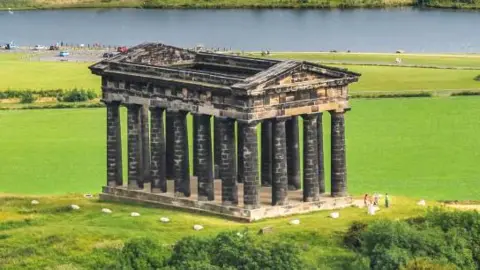Aerial view of the monument. It is on top of a hill and is made up of 18 large stone columns in a rectangle supporting an ornate triangular roof, although the roof is totally open.