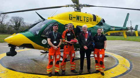 Wiltshire and Bath Air Ambulance Charity Four people smiling in front of a helicopter